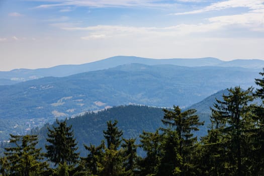 Beautiful green and blue panorama of layers of mountains and trees and some fields seen from top of viewing tower at highest mountain in this area