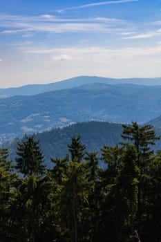 Beautiful green and blue panorama of layers of mountains and trees and some fields seen from top of viewing tower at highest mountain in this area