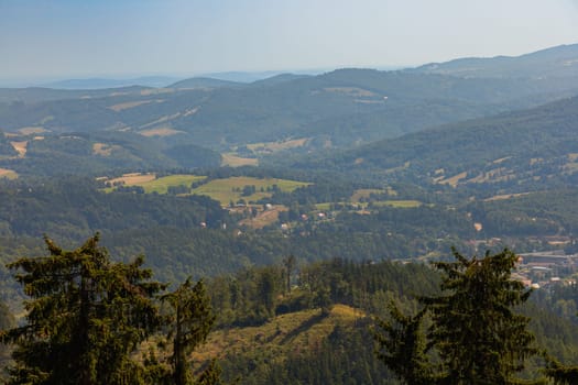 Beautiful green and blue panorama of layers of mountains and trees and some fields seen from top of viewing tower at highest mountain in this area