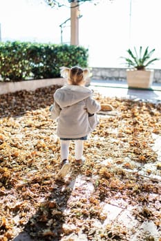 Little girl walks on fallen dry leaves in the garden. Back view. High quality photo