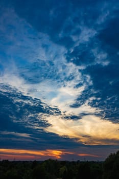 Beautiful cloudy sunset at afternoon with dark cloudy sky over high green trees and bushes