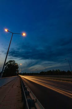 Long streaks of light made by riding cars on the road on the bridge at cloudy afternoon