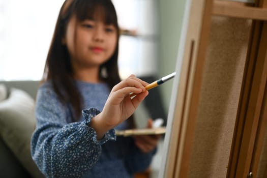 Select focus on schoolgirl painting picture on canvas, enjoying leisure weekend activity at home.