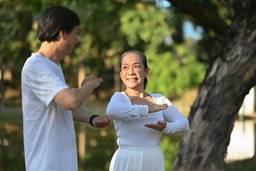 Active middle age couple in white clothing working out with Tai Chi in the park. Health care and wellbeing concept