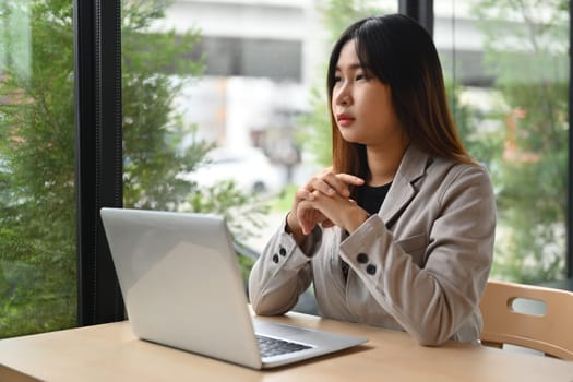 Thoughtful young woman sitting at workplace looking away dreaming of future or thinking on new ideas