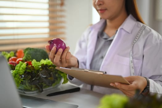 Nutritionist in white coat working on a diet plan at desk fresh vegetable and fruit. Health care concept
