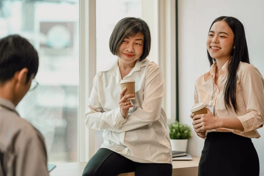 Friendly senior businesswoman taking coffee break after conference with younger colleagues