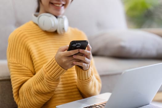 Mockup image of a woman holding mobile phone with blank desktop white screen and headphone while lying on a sofa at home.