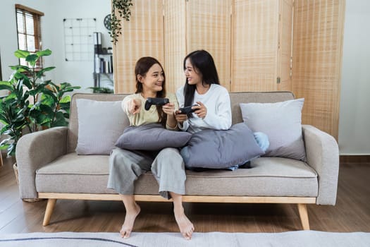 Young woman lesbian couple sitting on the comfortable sofa and playing game console while spending time together in living room at home.