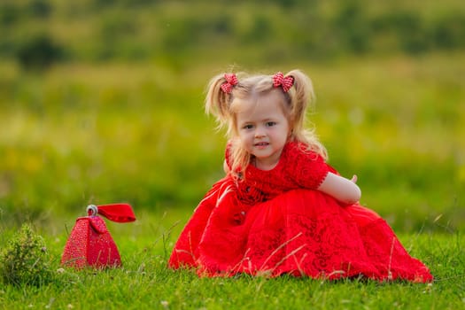 little girl in a red dress sits on a green lawn
