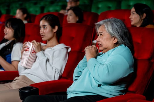 Asian senior woman look scary or panic during watch movie in cinema theater and other in the hall also express the same acting.