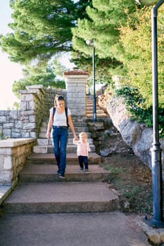 Mom and little girl walk up the steps in the park from the hill holding hands. High quality photo