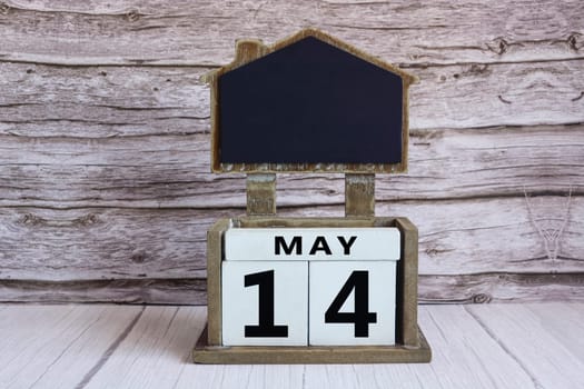 Chalkboard with May 14 calendar date on white cube block on wooden table.