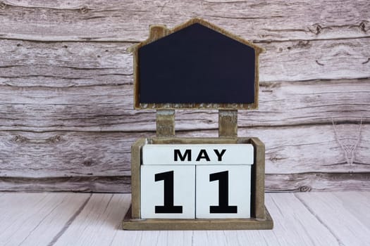 Chalkboard with May 11 calendar date on white cube block on wooden table.