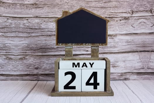 Chalkboard with May 24 calendar date on white cube block on wooden table.