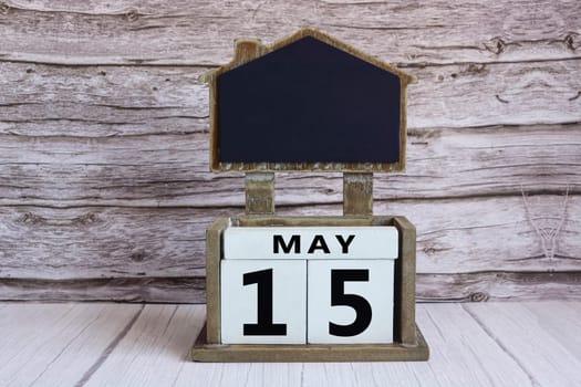 Chalkboard with May 15 calendar date on white cube block on wooden table.