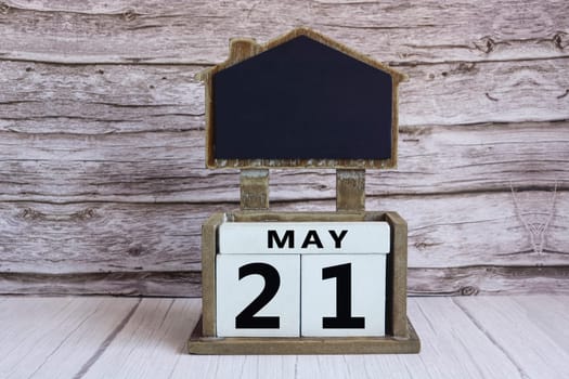 Chalkboard with May 21 calendar date on white cube block on wooden table.