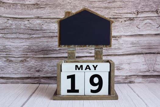 Chalkboard with May 19 calendar date on white cube block on wooden table.