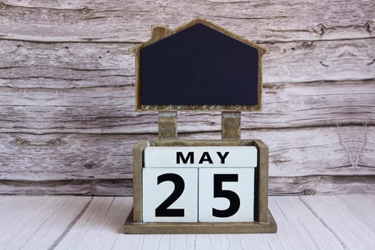 Chalkboard with May 25 calendar date on white cube block on wooden table.