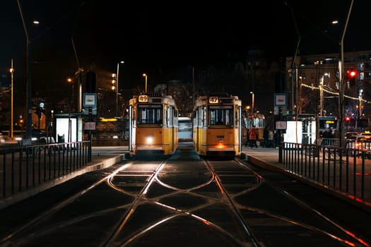 Tramways stand on tram rails in evening time. Trams stop on deserted street in city center illuminated by streetlamps awaiting for morning travellers