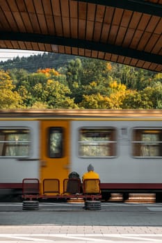 Train arrives at station where passenger sits waiting for journey. Man watches train depart from station sitting on bench near railroad tracks