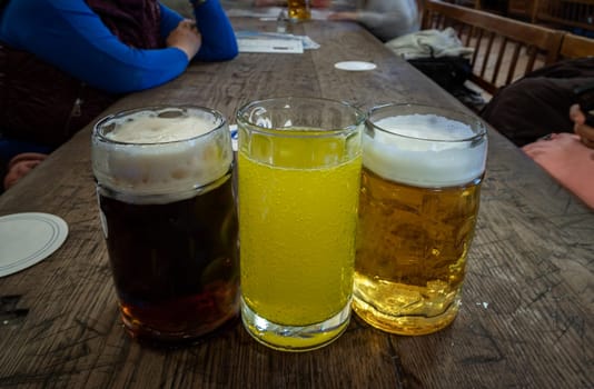 Three glasses of different types of cold tasty beer are in a row on a wooden table in a restaurant. Table for company of friends, Space for text, Selective focus.