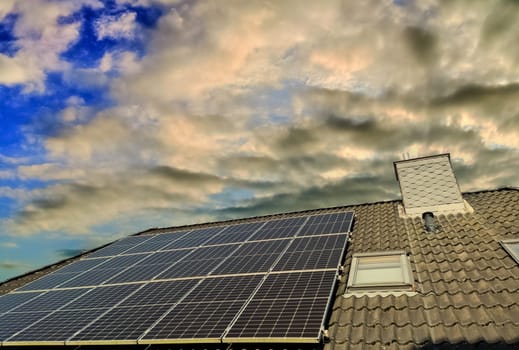 Solar panels producing clean energy on a roof of a residential house with a sunset sky