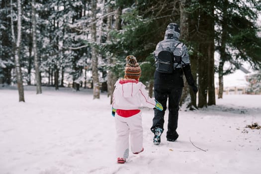 Little girl follows her mother through snowdrifts in a snowy forest. Back view. High quality photo