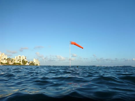 Flag pole with wind sock rises above the wavy waters of Waikiki, Hawaii.