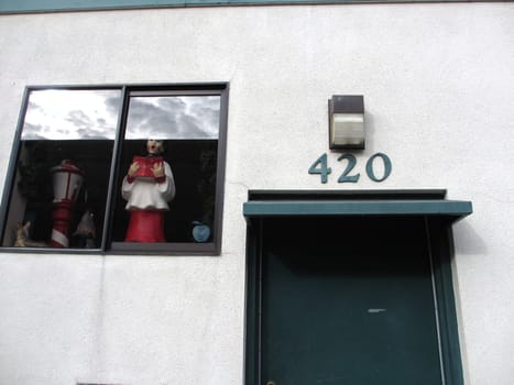 San Francisco - December 28, 2011: Quirky and whimsical window display at address 420, featuring a red fire hydrant and a figurine wearing red and white clothing. The photo shows the light-colored building wall, the dark green door and door frame, and the outdoor light fixture above the address number.