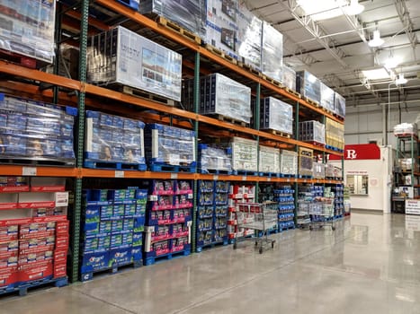 Honolulu - December 11, 2018: Aisle in Costco Honolulu with various products on display, including bottled water, soda, and snacks. The products are arranged on blue metal shelves that reach the ceiling. The ceiling is white with hanging lights and the floor is concrete. The photo shows a red wall with a white “R” on it in the background.