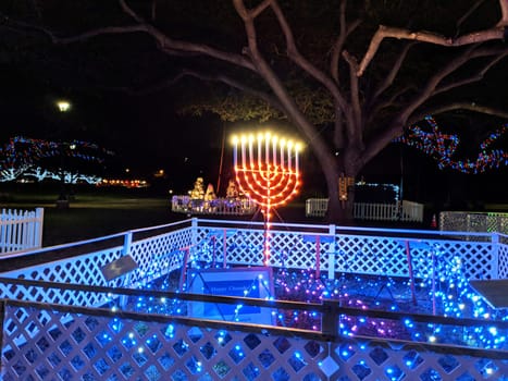 Honolulu - December 18, 2017: Large red menorah with blue lights on a white platform in a park-like setting outside Honolulu Hale, the seat of government for the City and County of Honolulu. The photo shows the dark sky and the beige building with two small lights in the background.
