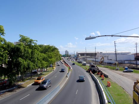 Sam Juan, Puerto Rico - January 13, 2009: Highway in San Juan, Puerto Rico, the capital and largest city of the U.S. territory. The highway is a divided highway with a concrete median and a street light hanging over it. The highway has a few cars on it, including a yellow taxi, a common mode of transportation in the city. The background consists of buildings and a few palm trees, showing the urban and tropical aspects of San Juan. The sky is blue with some clouds, creating a contrast with the highway and the buildings.