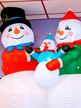 Honolulu - November 18, 2023: Three inflatable snowmen decorations at a fun factory. The snowmen are different sizes and are wearing different hats and scarves. The photo shows a purple wall with a window in the background.
