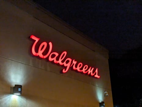 Honolulu - August 25, 2023:  Walgreens logo, a red cursive writing, on a beige building at night. The logo is lit up and stands out against the dark sky. 