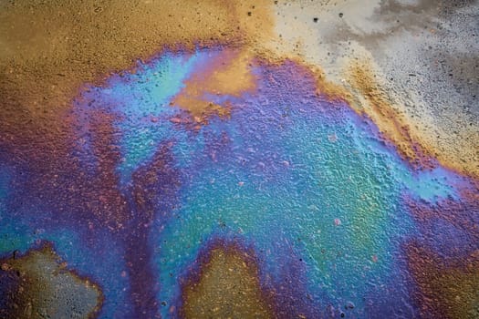 Multi-colored poisonous spots of spilled gasoline on wet pavement during rain. Rain blurred the car oil from a malfunctioning car in a parking lot
