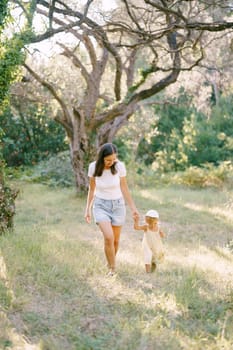 Mom and a little girl, holding hands, walk in the park and look at their feet. High quality photo