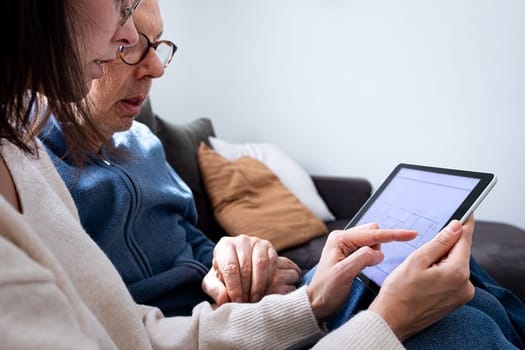 Close up of senior man and young woman using digital tablet together sitting on sofa in living room. Family members sharing technology. Lifestyle and technology concept.