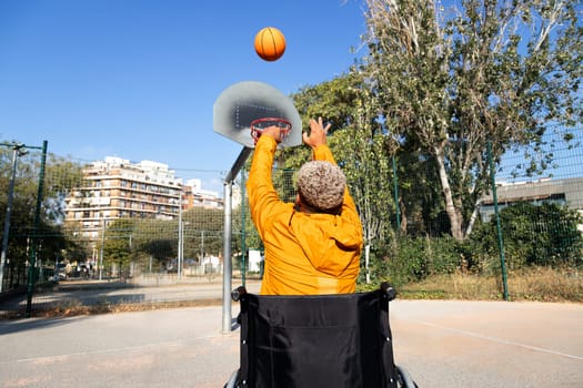 Rear view of African American man in a wheelchair throwing basketball in court playing alone. Sports and disabilities concept.