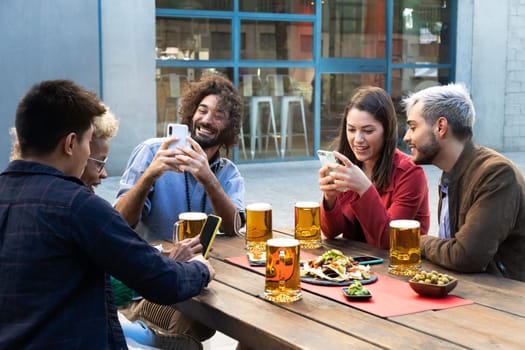 Group of multiracial friends using mobile phones, taking photos and using social media in a bar. Social media addiction concept.