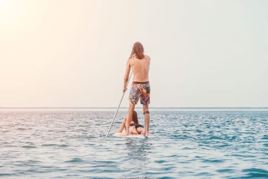 Sea woman and man on sup. Silhouette of happy young woman and man, surfing on SUP board, confident paddling through water surface. Idyllic sunset. Active lifestyle at sea or river