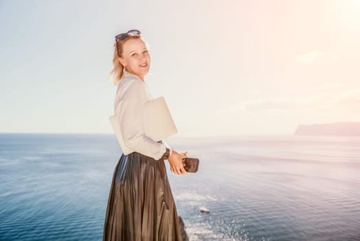 Digital nomad, Business woman working on laptop by the sea. Pretty lady typing on computer by the sea at sunset, makes a business transaction online from a distance. Freelance remote work on vacation