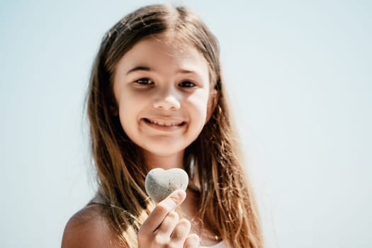 Female hand holding a stone in the shape of a heart against the background of the sea