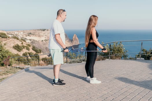 Happy Middle aged couple or friends practicing nordic walking in park near sea. Mature couple with trekking poles walking, practicing Nordic walking outdoors. Aging youthfully and sport concept.