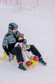 Smiling mother and little girl riding down the slope on a sleigh. High quality photo