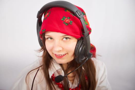 Portrait of young girl in red scarf, large headphones with microphone and black glasses. Woman who is radio or television presenter in workplace. Funny female telecom operator. Freelancer at work
