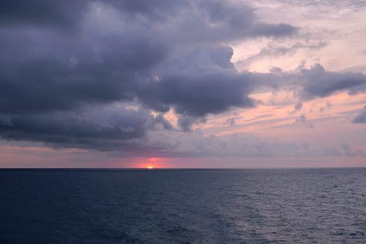 Sunset over the mediterranean sea on a cloudy day.Ocean, rain clouds, horizon line, empty space with no one, cold tones, blue, orange sunshine