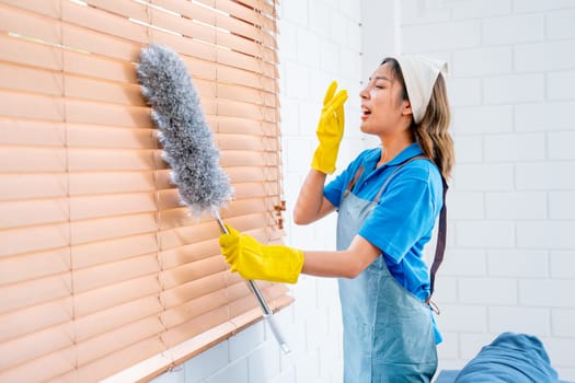 Asian housekeeper or housemaid action of sneeze during clean curtain or shade of windows with feather duster in living room with day light.