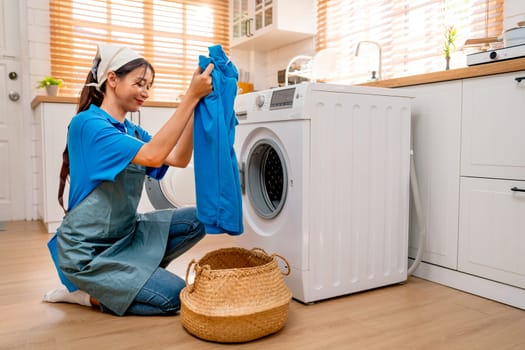 Asian housekeeper or housemaid hold and check blue cloth before put into washing machine during home service to customer.