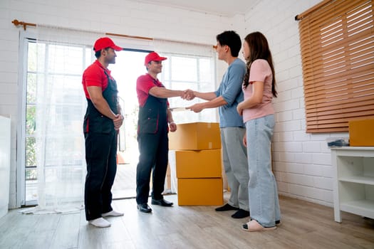 Asian man stand with his wife also shake hands to delivery men during process to send product to customer house.